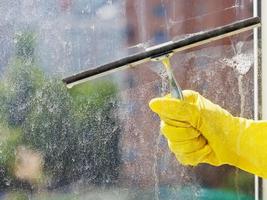 Hand im gelben Handschuh, der das Fenster mit einem Rakel abwischt foto