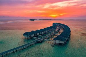 erstaunlicher sonnenunterganghimmel und reflexion über ruhiges meer, malediven strandlandschaft von luxus über wasserbungalows. exotische landschaft von sommerferien und urlaubshintergrund. foto