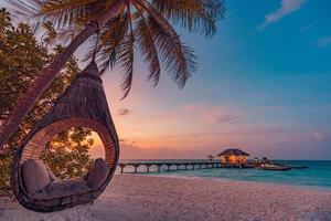 tropischer sonnenuntergangstrandhintergrund, sommerinsellandschaft mit strandschaukel oder hängematte und sandromantischem seestrand. schöner strandszenenurlaub oder sommerferienkonzept. Flitterwochen, Romantik-Resort foto