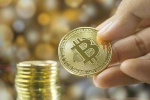 Stapel von Gold-Bitcoin-Münzen in der Hand mit goldenem Bokeh-Hintergrund. foto