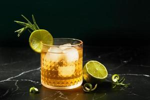 alkoholischer oder alkoholfreier cocktail mit limette und rosmarin auf einem dunklen marmortisch foto