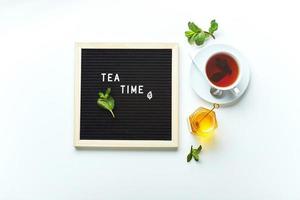 Teezeit. Schwarzes Briefbrett mit Text auf Marmortisch mit Glastasse Tee mit Minzblättern