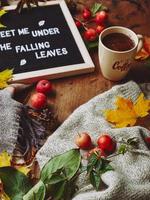 Herbst-Flatlay mit Briefbrett, kuscheligem Pullover und Schal, Tasse Kaffee, bunten Blättern und kleinen Äpfeln auf Holzhintergrund foto