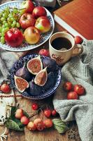 gericht mit feigen, äpfeln und trauben und einer tasse kaffee auf einem hölzernen hintergrund mit warmer gemütlicher strickwaren, herbstblättern und äpfeln.