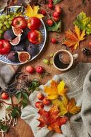 Teller mit Feigen, Äpfeln und Trauben und Tasse Kaffee auf Holzhintergrund mit warmem Pullover, Schal, Herbstlaub und Äpfeln. Herbsthintergrund, Draufsicht. foto