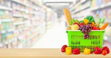 einkaufskorb gefüllt mit obst und gemüse auf holztisch mit supermarkt-lebensmittelgeschäft verschwommener defokussierter hintergrund mit bokeh-licht foto