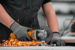 schwerindustrie-fabrikinnenraum mit industriearbeiter, der winkelschleifer verwendet und ein metallrohr schneidet. Auftragnehmer in der Herstellung von Metallstrukturen für Sicherheitsuniformen und Schutzhelme. foto