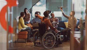 Behinderter Geschäftsmann im Rollstuhl bei der Arbeit in einem modernen Open-Space-Coworking-Büro mit Team, das Virtual-Reality-Googles-Drohnenunterstützungssimulation verwendet foto