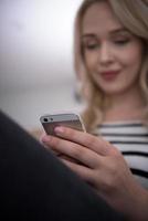 Frau sitzt mit Handy auf Sofa foto