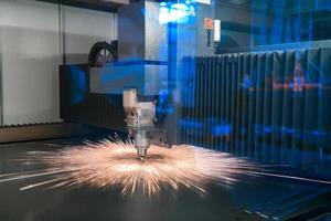 Funken fliegen aus Maschinenkopf für die Metallbearbeitung Lasermetall auf metallurgischem Anlagenhintergrund. herstellung fertiger teile für das konzept der automobilproduktion foto