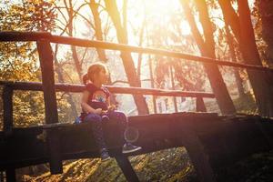 Kleines Mädchen, das sich an einem sonnigen Herbsttag auf einer Holzbrücke entspannt. foto