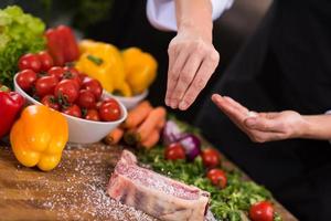 koch, der salz auf eine saftige scheibe rohes steak legt foto