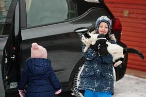 Junge mit Katze auf Händen gegen Auto im Hof des Hauses im Winter. foto