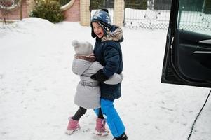 bruder mit schwester spielen im winter gegen das aufladen von elektroautos im hof des hauses. foto