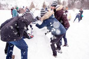 Gruppe junger Leute, die einen Schneemann bauen foto