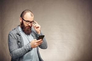 bärtiger mann mit brille, der schlechte nachrichten auf dem handy liest foto