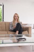 Frau sitzt mit Handy auf Sofa foto