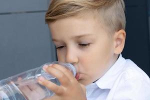 Süßer Junge trinkt Wasser aus einer Flasche. foto