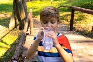 Durstiger Junge trinkt Wasser aus einer Flasche in der Natur. foto