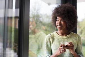 Afroamerikanerin trinkt Kaffee und schaut aus dem Fenster foto