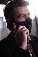 geschäftsmann, der eine medizinische gesichtsmaske des coronavirus trägt, während er das smartphone benutzt foto