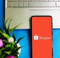 faridpur, bangladesch 21. september 2022 das shopee-logo auf dem smartphone-bildschirm wird auf der laptop-tastatur auf blauem schreibtischhintergrund platziert. foto