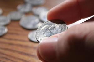 hand, die eine viertelmünze in amerikanischer währung aufhebt, die auf dem holzboden verteilt ist foto