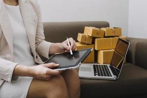 Start-up-KMU-Kleinunternehmer einer freiberuflich tätigen Asiatin, die einen Laptop mit Box verwendet fröhlicher Erfolg Asiatin ihre Hand hebt die Online-Marketing-Verpackungsbox und das Konzept der KMU-Ideenlieferung an foto