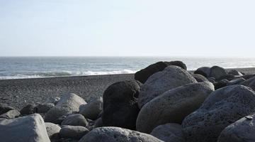 Kiesel und Felsen am Strand von Reynisfjara, Island, mit dem Meer im Hintergrund foto