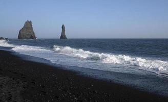 Wellen am schwarzen Strand von Reynisfjara, Island, mit Felsformationen im Hintergrund foto