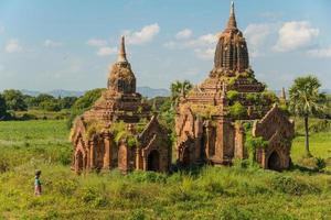 die Landschaftsansicht des alten Tempels in der archäologischen Stätte Bagan mit Einheimischen, die auf dem Gebiet der Landwirtschaft spazieren gehen. foto