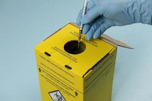 Sammelbox für kontaminierte Krankenhausabfälle mit Hand, die eine Spritze platziert foto