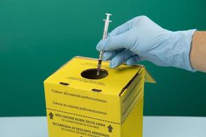 Sammelbox für kontaminierte Krankenhausabfälle mit Hand, die eine Spritze platziert foto