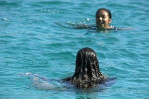 mexikanisches latina-mädchen mit schwarzen haaren, das in kristallklarem meerwasser schwimmt foto