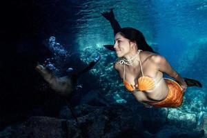 Meerjungfrau, die mit einem Siegel im tiefblauen Meer unter Wasser schwimmt foto