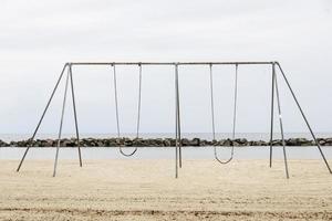 Metallschaukeln an einem Sandstrand in der Nähe des Ozeans foto