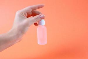 weibliche Hand mit kosmetischer Flasche auf Grapefruit-farbigem Hintergrund foto