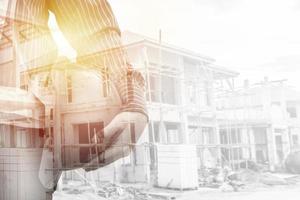 bauingenieurarbeiter halten helmdoppelbelichtung mit neuem wohnhaus im bau auf der baustelle foto