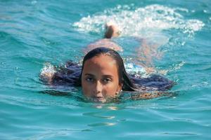 mexikanisches latina-mädchen mit schwarzen haaren, das in kristallklarem meerwasser schwimmt foto