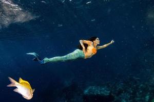 Meerjungfrau, die unter Wasser im tiefblauen Meer schwimmt foto