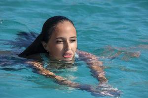 mexikanisches latina-mädchen mit schwarzen haaren, das in kristallklarem meerwasser schwimmt foto