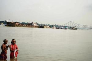 Zwei Personen beten für Gott im Ganga Ghat von Kalkutta und zeigen die Howrah-Brücke im Bakcground während des Mahalaya-Tarpan. Kalkutta, Westbengalen, 25. September 2022 foto