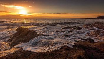 Wellen, die während des Sonnenuntergangs an Land krachen foto