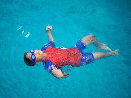 Junge, der einen Badeanzug und eine Brille trägt, schwimmt mitten im Pool mit blauem Wasserhintergrund foto