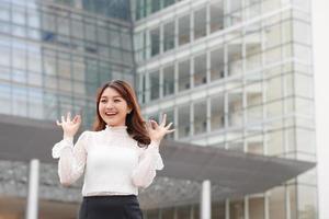 Schöne ernsthafte selbstbewusste junge Geschäftsfrau, die eine okay-Geste in einem Bürogebäude im Freien zeigt foto
