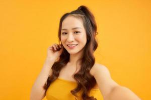 Porträt eines coolen, fröhlichen Mädchens, das ein Smartphone in der Hand hält und ein Selfie schießt, das auf orangefarbenem Hintergrund isoliert ist und den Wochenendurlaub genießt foto