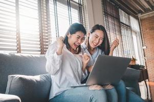 Beste Freundinnen asiatischer Frauen aufgeregt, während sie Laptop zu Hause benutzen foto