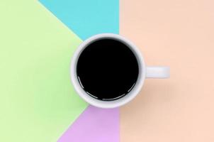 kleine weiße kaffeetasse auf texturhintergrund aus modepapier in pastellrosa, blau, korallen- und limettenfarben foto