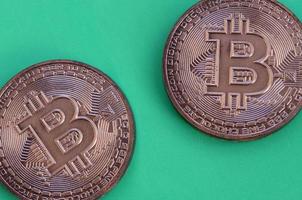Zwei Schokoladenprodukte in Form von physischen Bitcoins liegen auf einem grünen Kunststoffhintergrund. Modell der Kryptowährung in essbarer Form foto