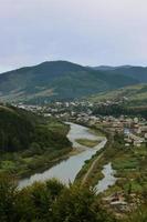 eine schöne aussicht auf das dorf mezhgorye, karpatengebiet. Viele Wohngebäude, umgeben von hohen Waldbergen und einem langen Fluss foto